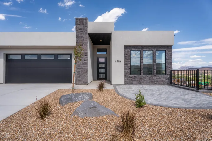 Contemporary exterior with stucco and stone accents, a modern garage door, paver patio, and xeriscape landscaping