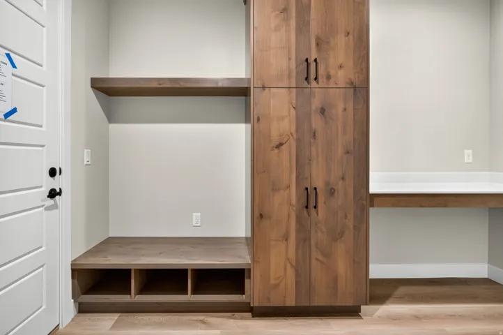 Custom wood-finish built-in cabinetry with multiple storage compartments and open shelving, featuring a lower bench unit with three cubbies and upper cabinet doors with metal hardware