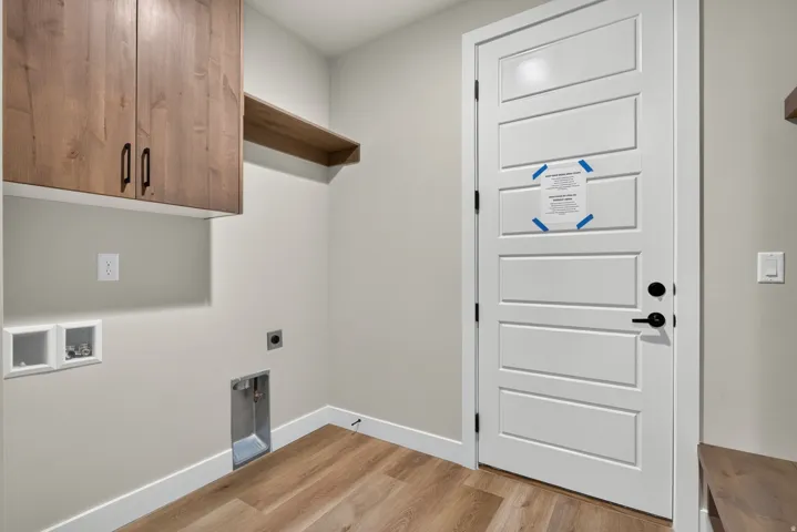 Laundry room featuring custom wood-finish cabinetry with ample storage, wood-finish flooring throughout, and a white six-panel entry door