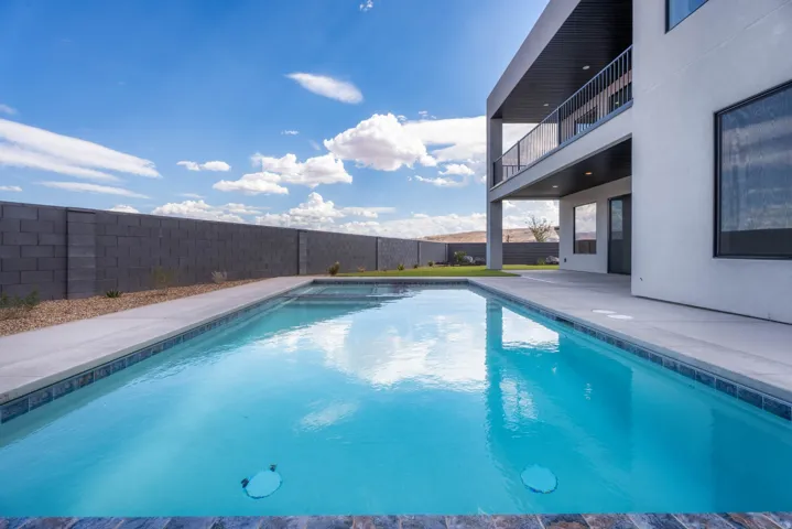 Newly constructed pool with a concrete surround, an upper-level balcony with a black metal railing, a covered patio, and a block wall perimeter