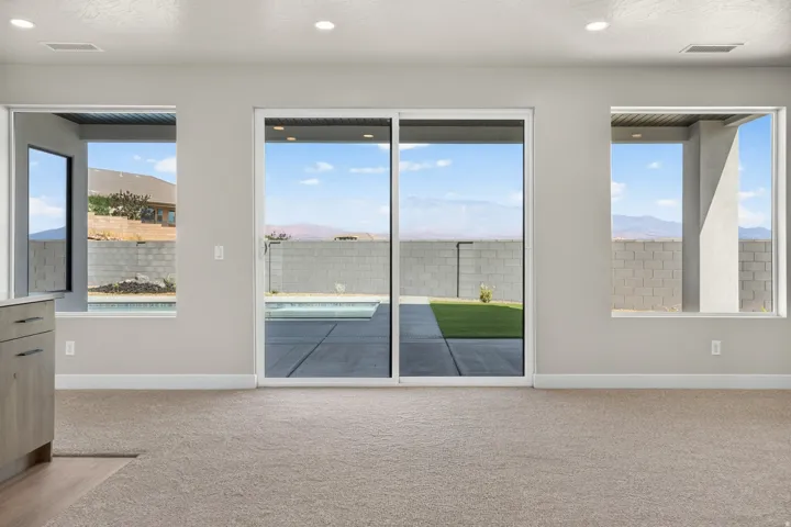 Sliding glass door opening to a concrete patio with a swimming pool, flanked by large windows with mountain scenery