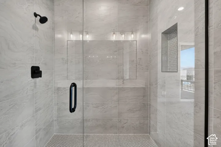 Walk-in shower with full-height tile surround, glass enclosure, matte black fixtures, and a recessed niche with mosaic tile