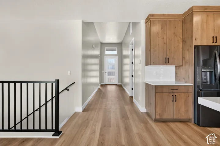 Wood-finish flooring throughout, light-toned cabinetry with dark hardware, white countertop, white subway tile backsplash, and black metal stair railing