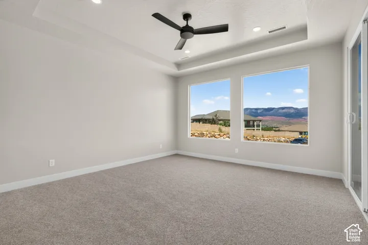 Recessed lighting, tray ceiling, ceiling fan, large windows, and carpeted flooring