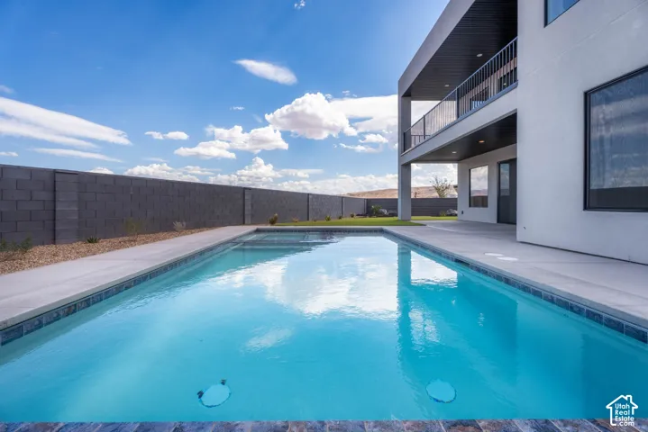 Newly constructed pool with a concrete surround, an upper-level balcony with a black metal railing, a covered patio, and a block wall perimeter