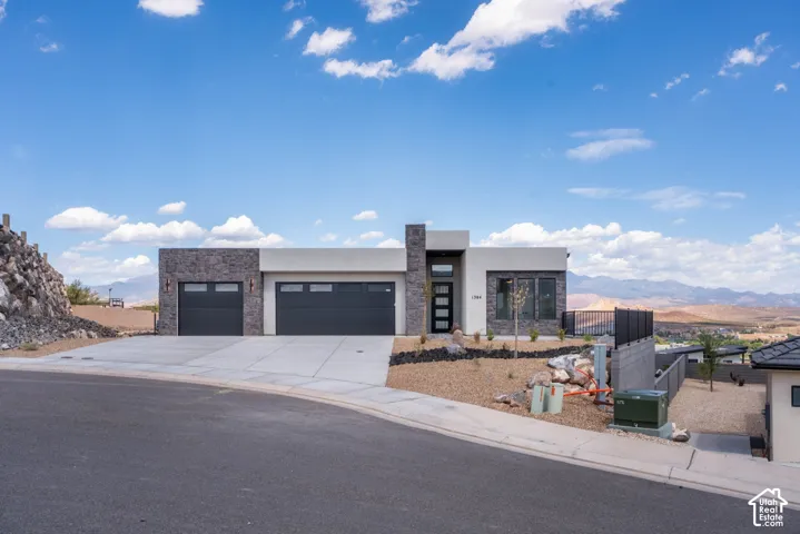 Modern architecture featuring a two-car garage, stone and stucco exterior, and multi-pane front entry door