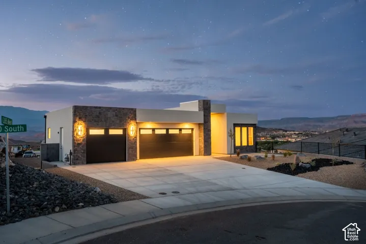 Contemporary stucco and stone exterior with integrated lighting, a concrete driveway, and attached garage