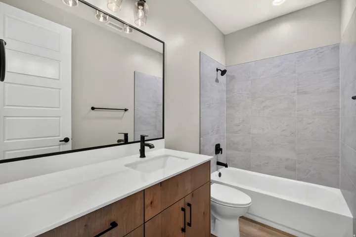 Spacious bathroom featuring a wood-finish vanity with white countertop, integrated sink, and matte black fixtures