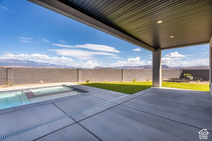 Covered patio with recessed lighting, integrated swimming pool, concrete patio decking, artificial turf lawn, and block wall fencing