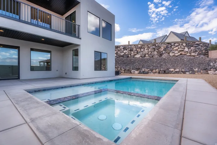 Outdoor pool with integrated spa, concrete patio, and upper-level balcony