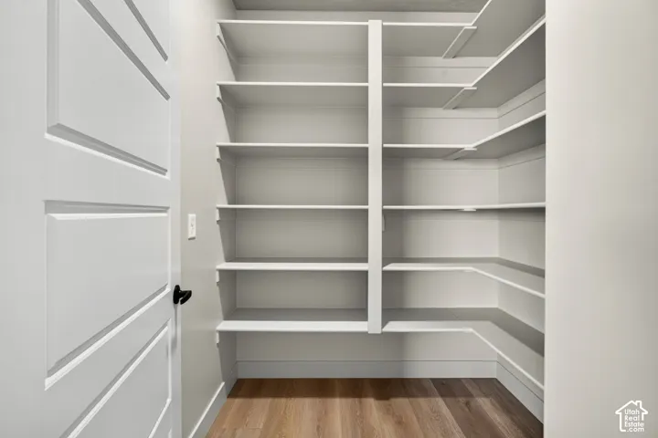 White paneled door with matte black hardware, L-shaped built-in shelving, wood-finish flooring, and light-toned walls