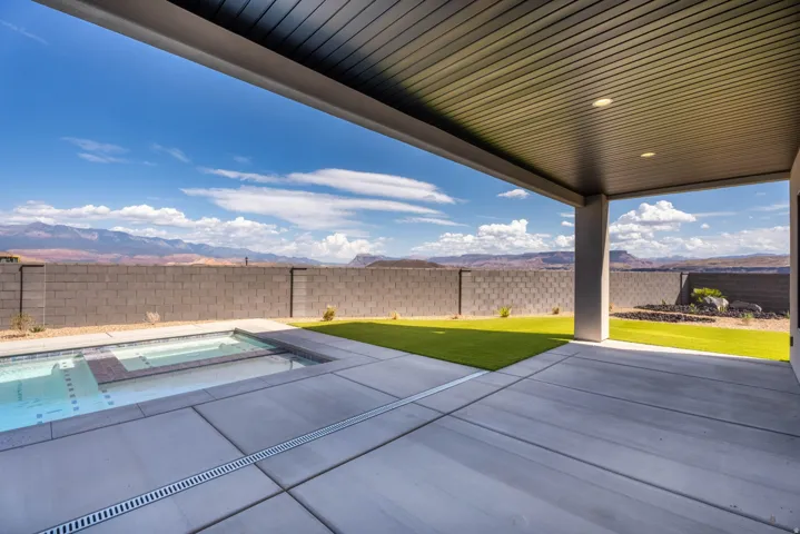Covered patio with integrated lighting, concrete paver patio, a swimming pool with an attached spa, and artificial turf