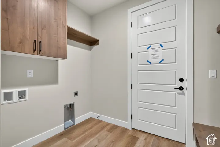 Laundry room featuring custom wood-finish cabinetry with ample storage, wood-finish flooring throughout, and a white six-panel entry door