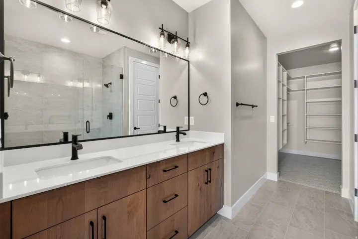 Dual vanity with wood-finish cabinetry, quartz countertops, and matte black fixtures