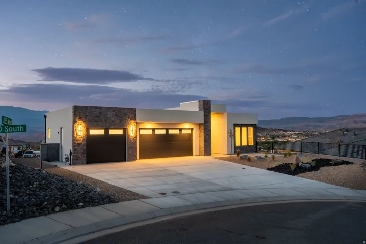 Contemporary stucco and stone exterior with integrated lighting, a concrete driveway, and attached garage