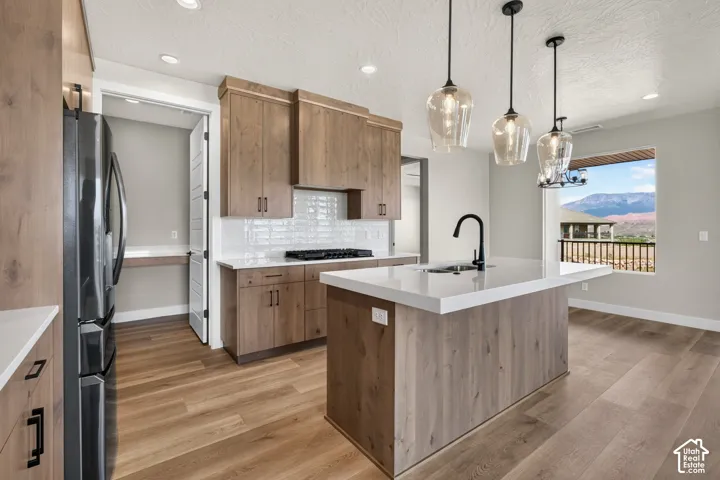 Kitchen featuring a large island with sink and integrated seating, wood-finish flooring, white countertops, and wood cabinetry