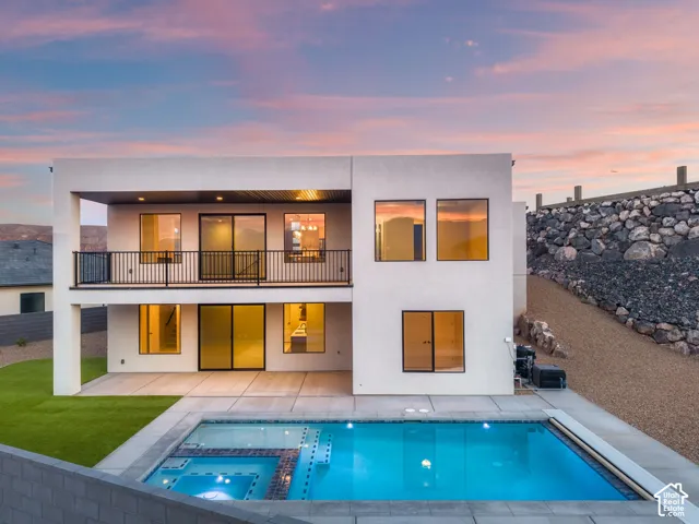 Modern exterior with multiple windows, second-story balcony with metal railing, ground-level patio, and an integrated pool and spa