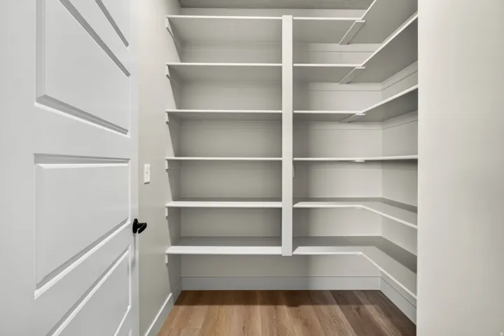 White paneled door with matte black hardware, L-shaped built-in shelving, wood-finish flooring, and light-toned walls