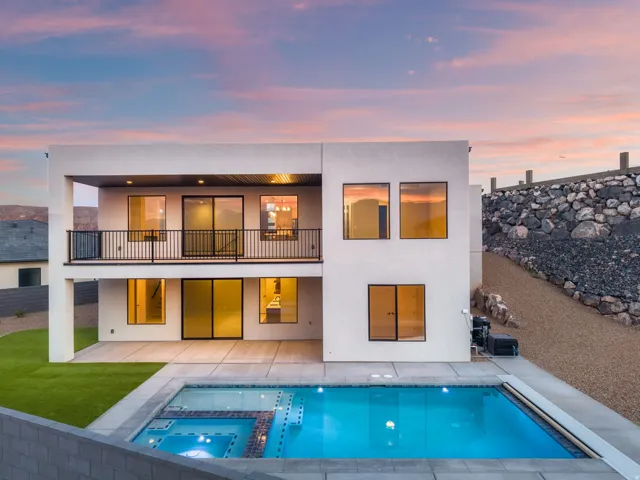 Modern exterior with multiple windows, second-story balcony with metal railing, ground-level patio, and an integrated pool and spa