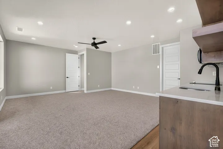 Recessed lighting, ceiling fan, neutral wall color, carpeted flooring, and a kitchen counter with a sink