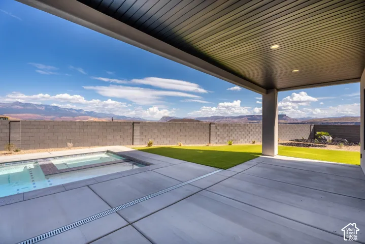 Covered patio with integrated lighting, concrete paver patio, a swimming pool with an attached spa, and artificial turf