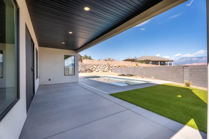 Covered patio with recessed lighting, integrated swimming pool, synthetic turf, and concrete block fencing