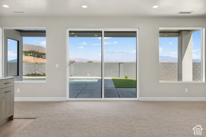 Sliding glass door opening to a concrete patio with a swimming pool, flanked by large windows with mountain scenery