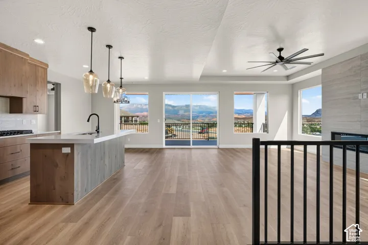 Open-concept living area featuring wood-finish flooring, a kitchen island with integrated sink, a built-in fireplace, a ceiling fan, and sliding glass doors to a balcony