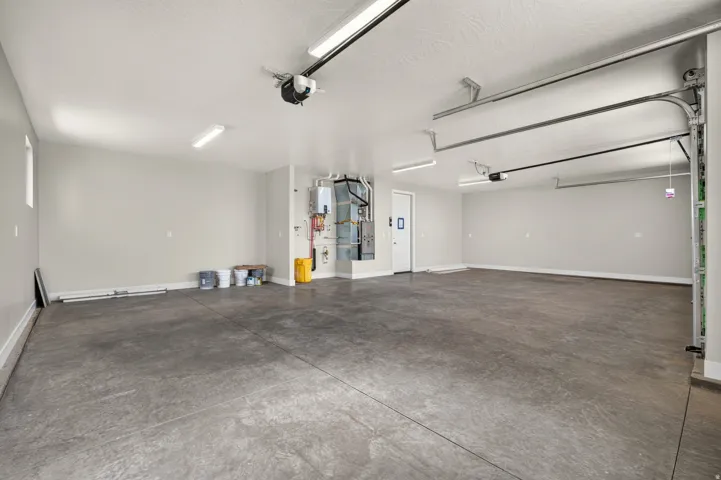 Spacious garage with concrete flooring, overhead lighting, and an accessible side entry door