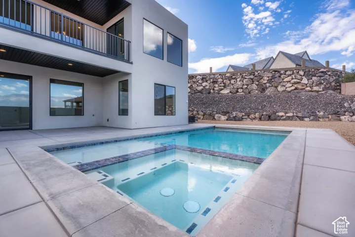 Outdoor pool with integrated spa, concrete patio, and upper-level balcony