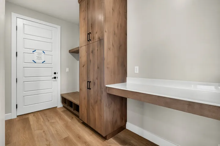 Wood-finish flooring, built-in wooden cabinetry, white panel door, built-in wooden bench with storage, white countertop surface