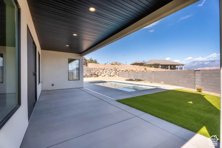 Covered patio with recessed lighting, integrated swimming pool, synthetic turf, and concrete block fencing