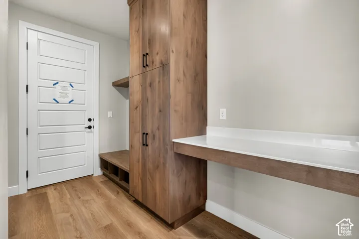 Wood-finish flooring, built-in wooden cabinetry, white panel door, built-in wooden bench with storage, white countertop surface