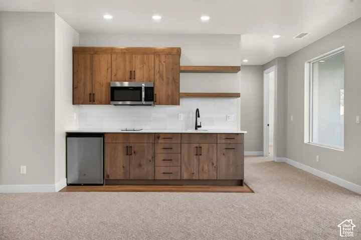 Kitchenette featuring wood-finish cabinetry, white subway tile backsplash, stainless steel microwave, and a compact refrigerator