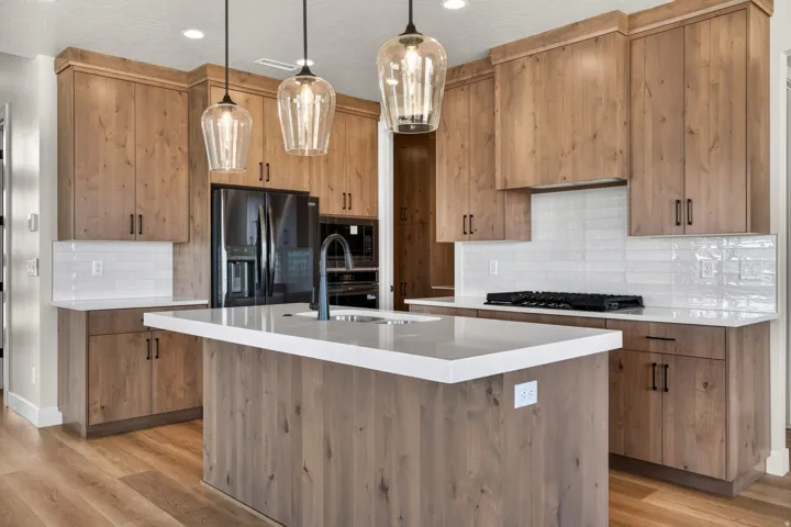 Kitchen featuring wood-finish cabinetry, white countertops, a central island with integrated sink, stainless steel appliances, and wood-finish flooring