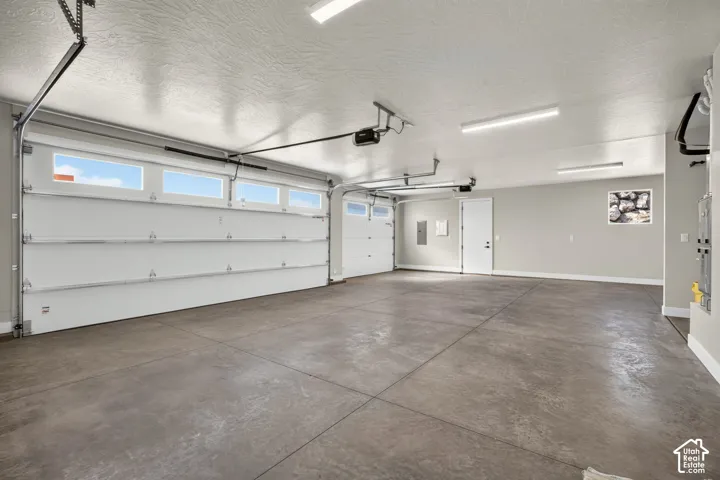 Spacious garage featuring a concrete floor, two white garage doors with upper windows, and flush-mounted ceiling lights