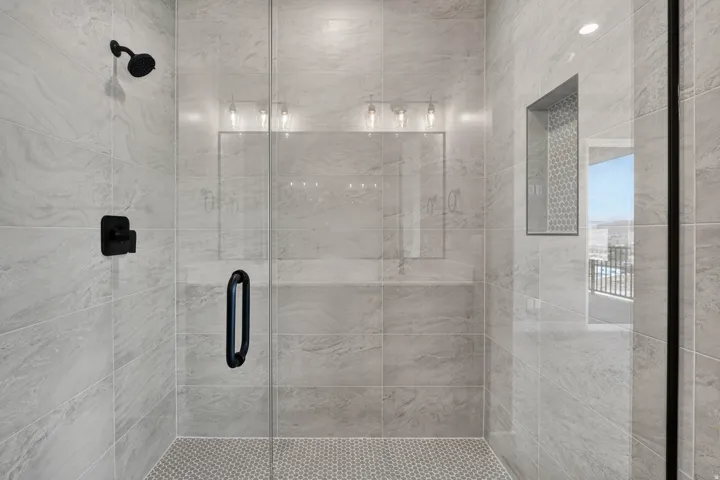 Walk-in shower with full-height tile surround, glass enclosure, matte black fixtures, and a recessed niche with mosaic tile
