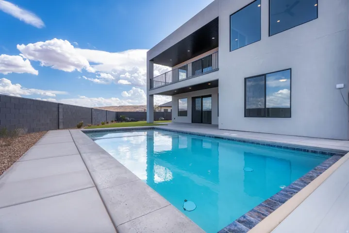 Contemporary stucco exterior with expansive windows, an upper-level balcony with metal railing, and a ground-level patio with sliding glass doors