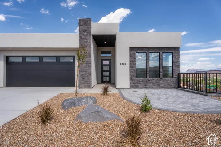 Contemporary exterior with stucco and stone accents, a modern garage door, paver patio, and xeriscape landscaping