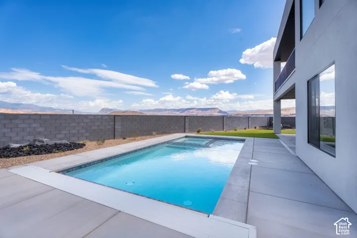 Rectangular inground pool with integrated spa, concrete patio surround, and an integrated pool cover