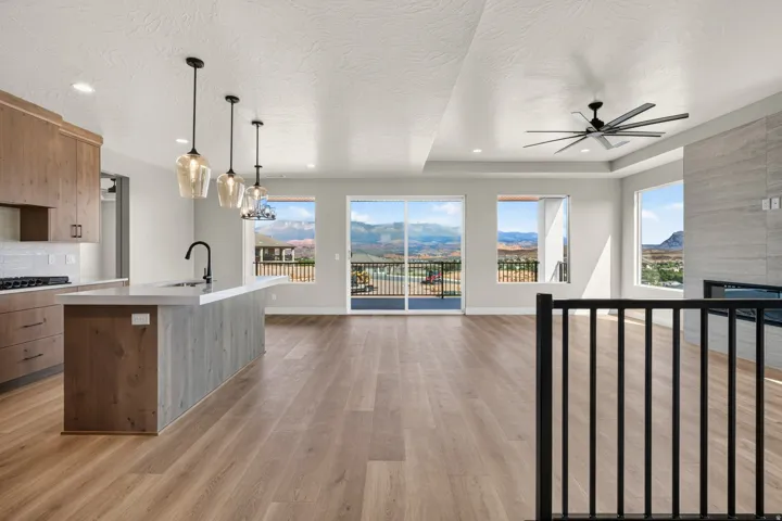 Open-concept living area featuring wood-finish flooring, a kitchen island with integrated sink, a built-in fireplace, a ceiling fan, and sliding glass doors to a balcony