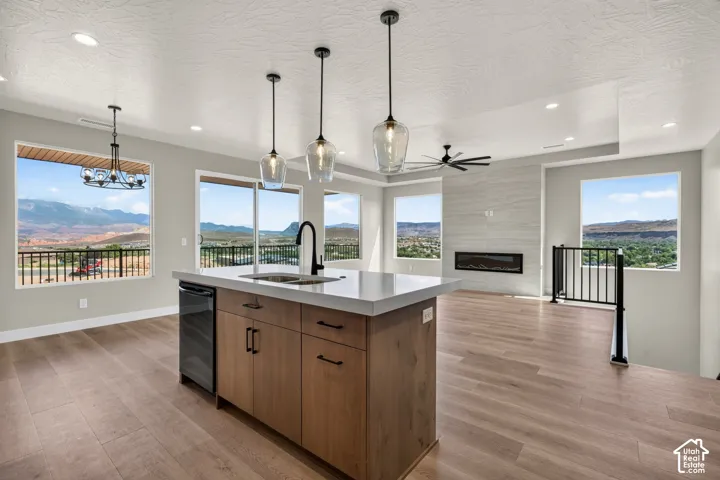 Kitchen island with undermount sink and beverage refrigerator, wood-finish flooring, linear fireplace with tiled surround, contemporary light fixtures, and black metal railing