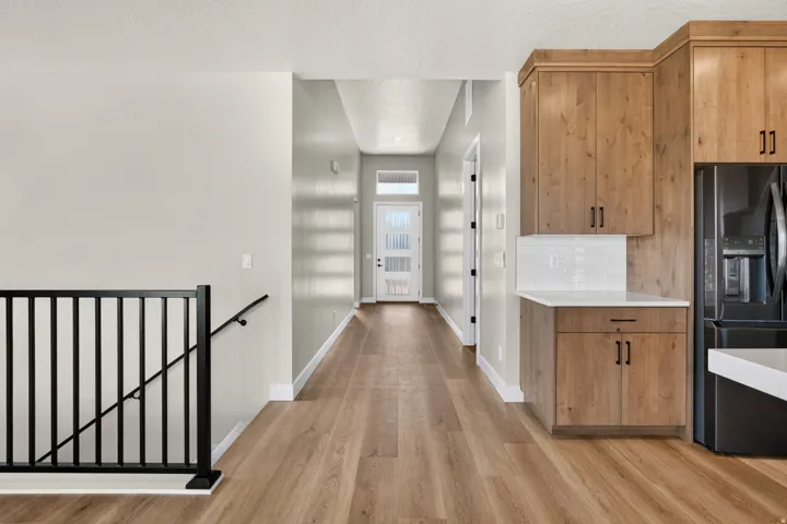 Wood-finish flooring throughout, light-toned cabinetry with dark hardware, white countertop, white subway tile backsplash, and black metal stair railing