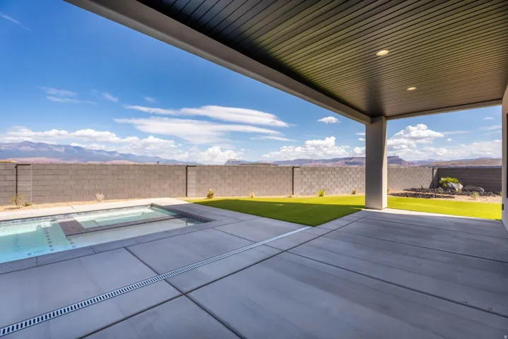 Covered patio with recessed lighting, integrated swimming pool, concrete patio decking, artificial turf lawn, and block wall fencing