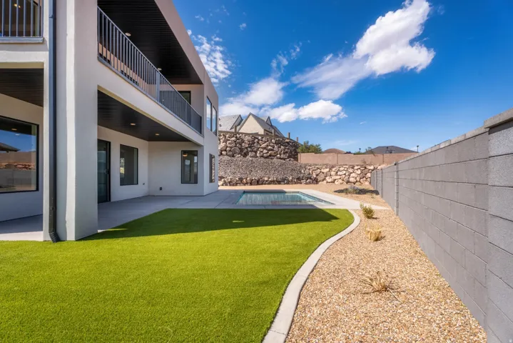Modern exterior design with a balcony, covered patio, artificial turf, gravel landscaping, and a swimming pool