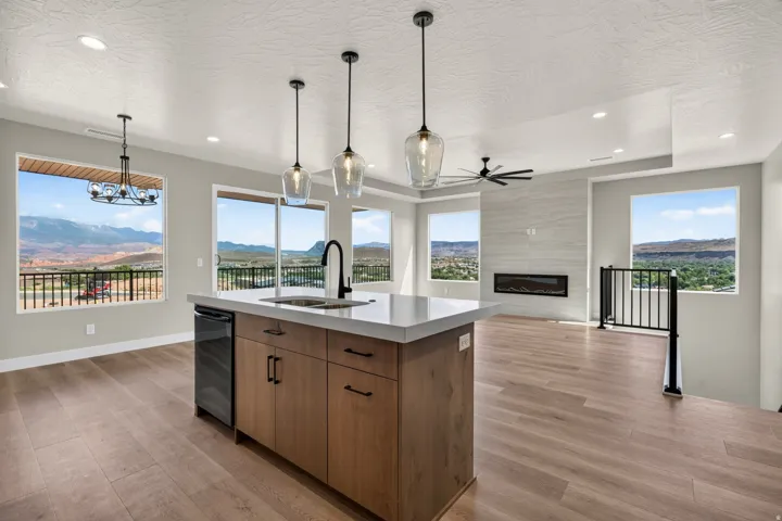 Kitchen island with undermount sink and beverage refrigerator, wood-finish flooring, linear fireplace with tiled surround, contemporary light fixtures, and black metal railing