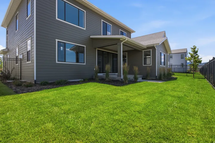 Expansive backyard featuring a manicured lawn, established landscaping, and a covered patio area
