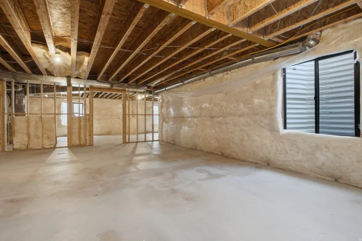 Unfinished lower level with concrete flooring, exposed wooden joists, framed interior walls, and an egress window