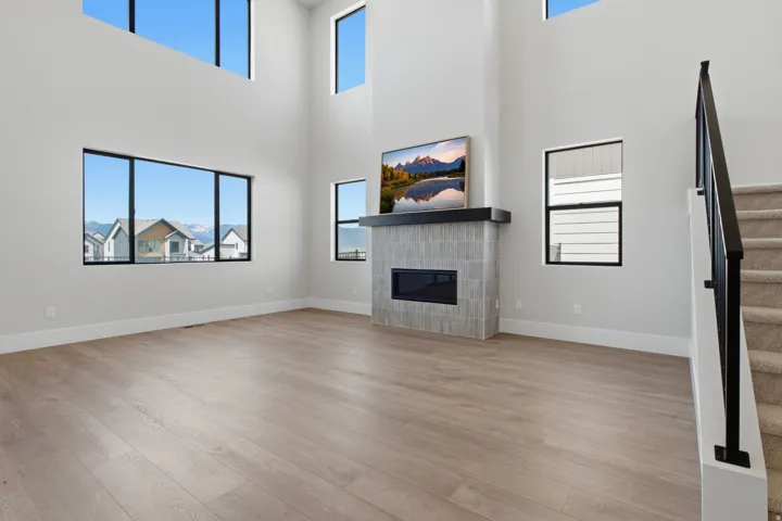 Double-height ceiling, tiled fireplace with mantel, black-framed windows, and carpeted stairs with metal railing