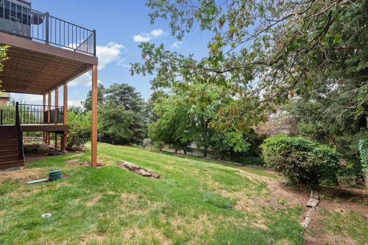 Expansive outdoor space featuring a two-story deck with black metal railings, a sloped grassy area, and mature trees